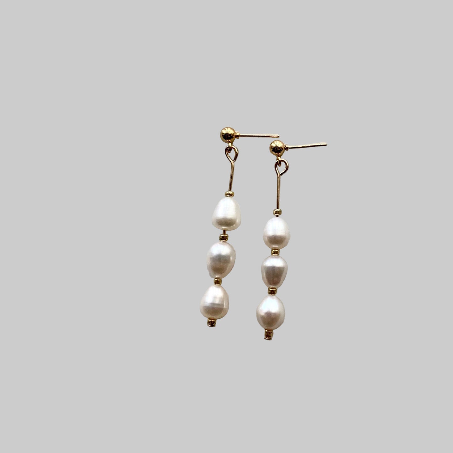 A pair of drop earrings featuring three freshwater pearls with gold bead accents on each end, mounted on a gold-colored earring wire.