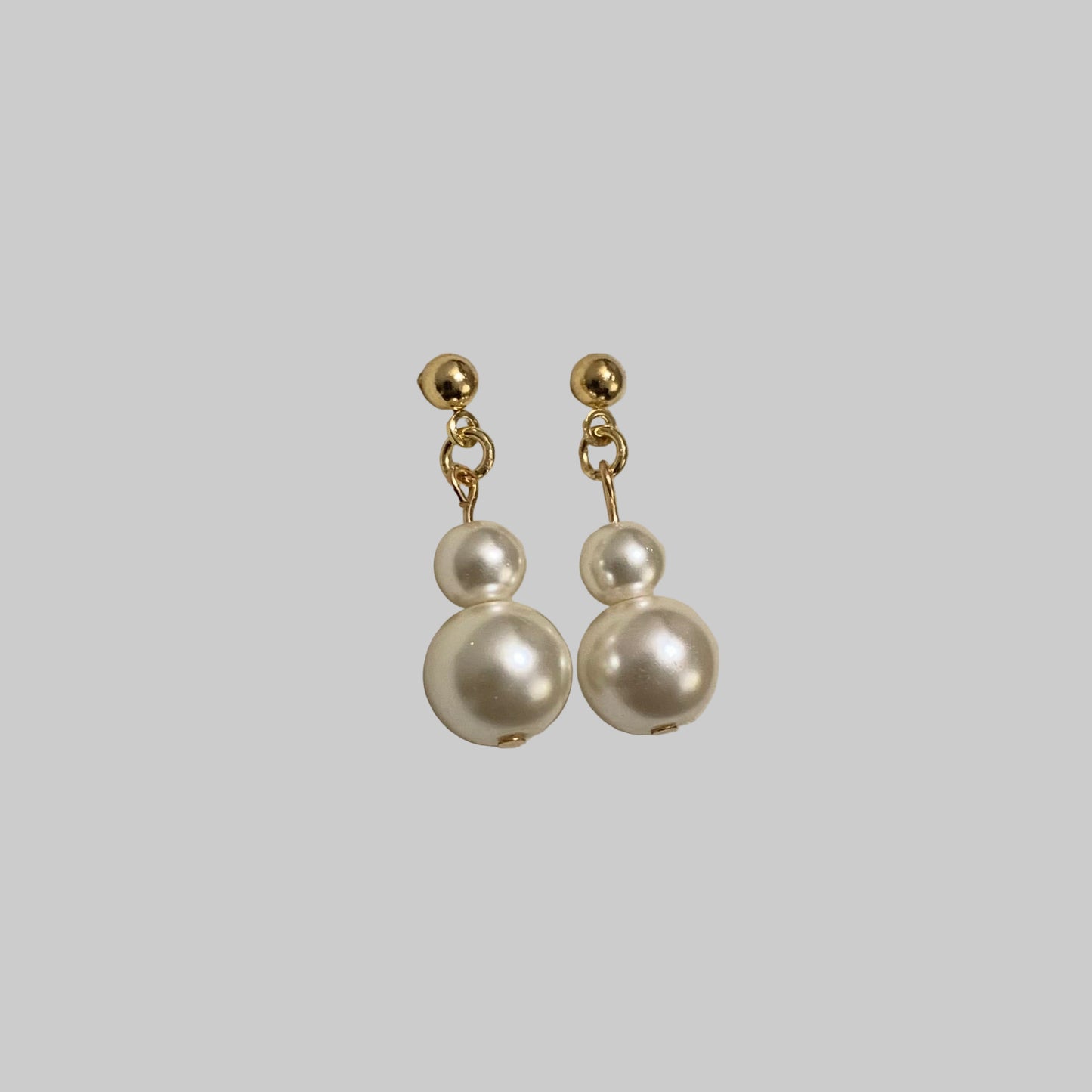 A pair of gold-plated double pearl drop earrings on a beige background.