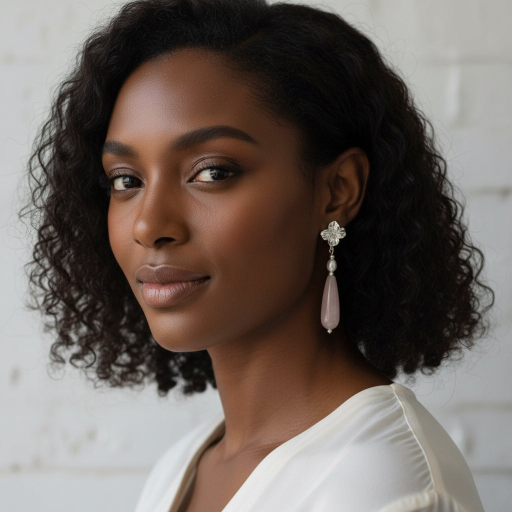 Pair of earrings with pink teardrop-shaped stones and silver floral tops on a light gray background