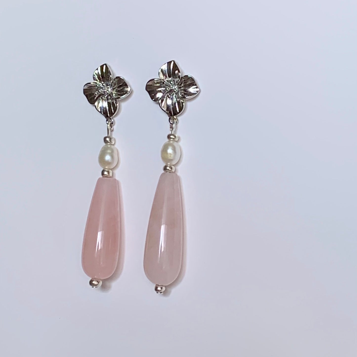 Pair of earrings with pink teardrop-shaped stones and silver floral tops on a light gray background