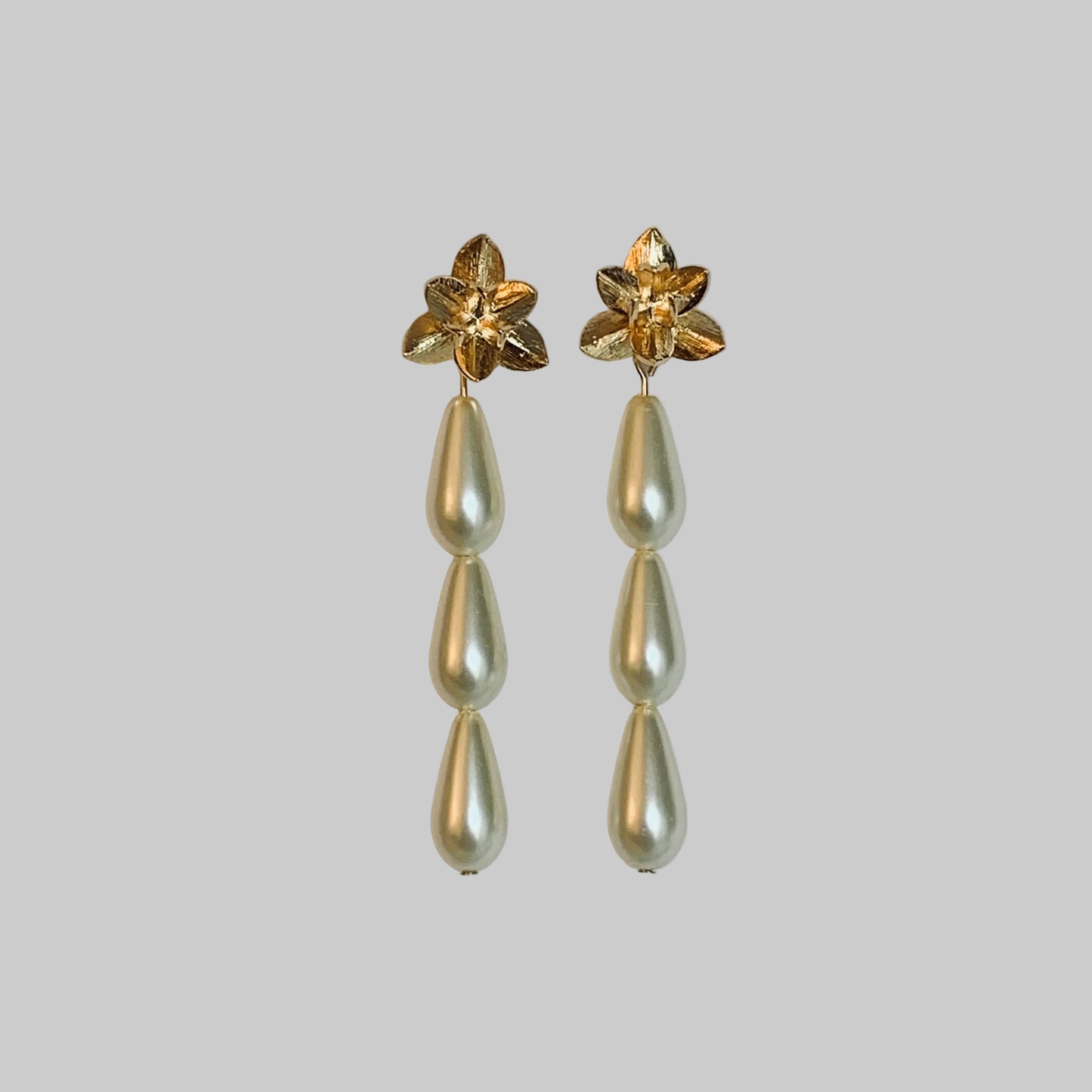 Pair of gold floral earrings with pearl drops on a light gray background