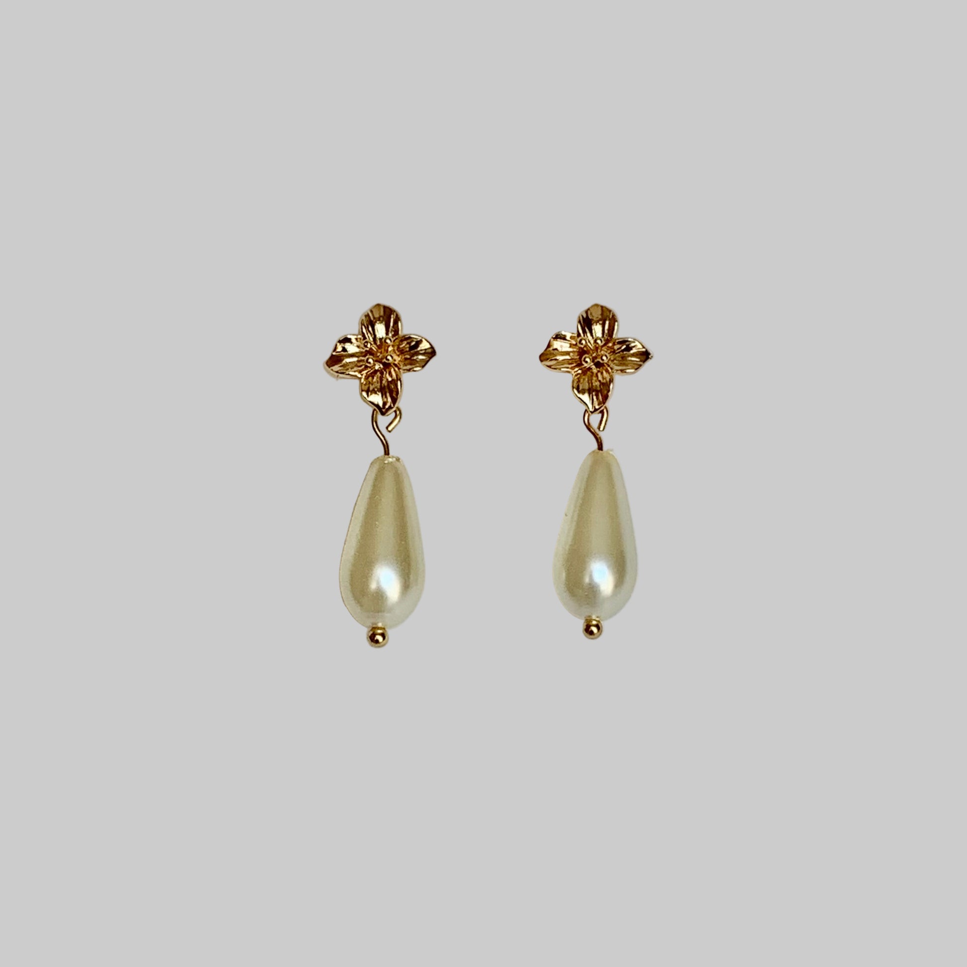 Gold earrings with pearl drops on a light gray background